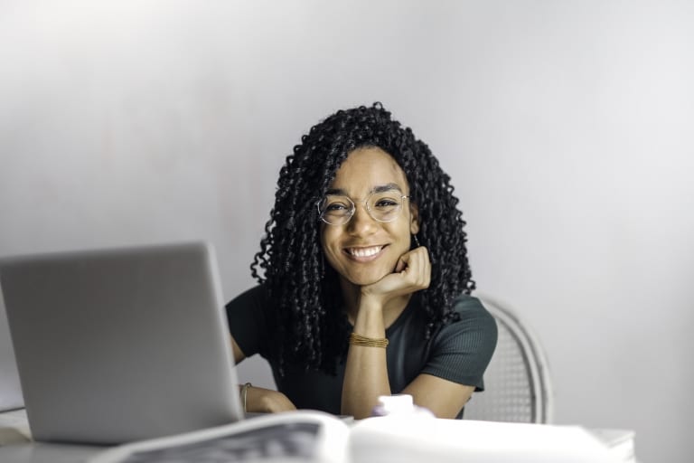happy ethnic woman sitting at table with laptop